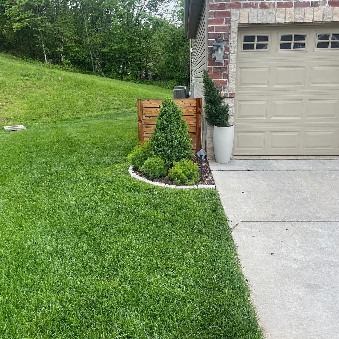 Well-manicured front yard with green grass, garden bed with plants, and a garage.