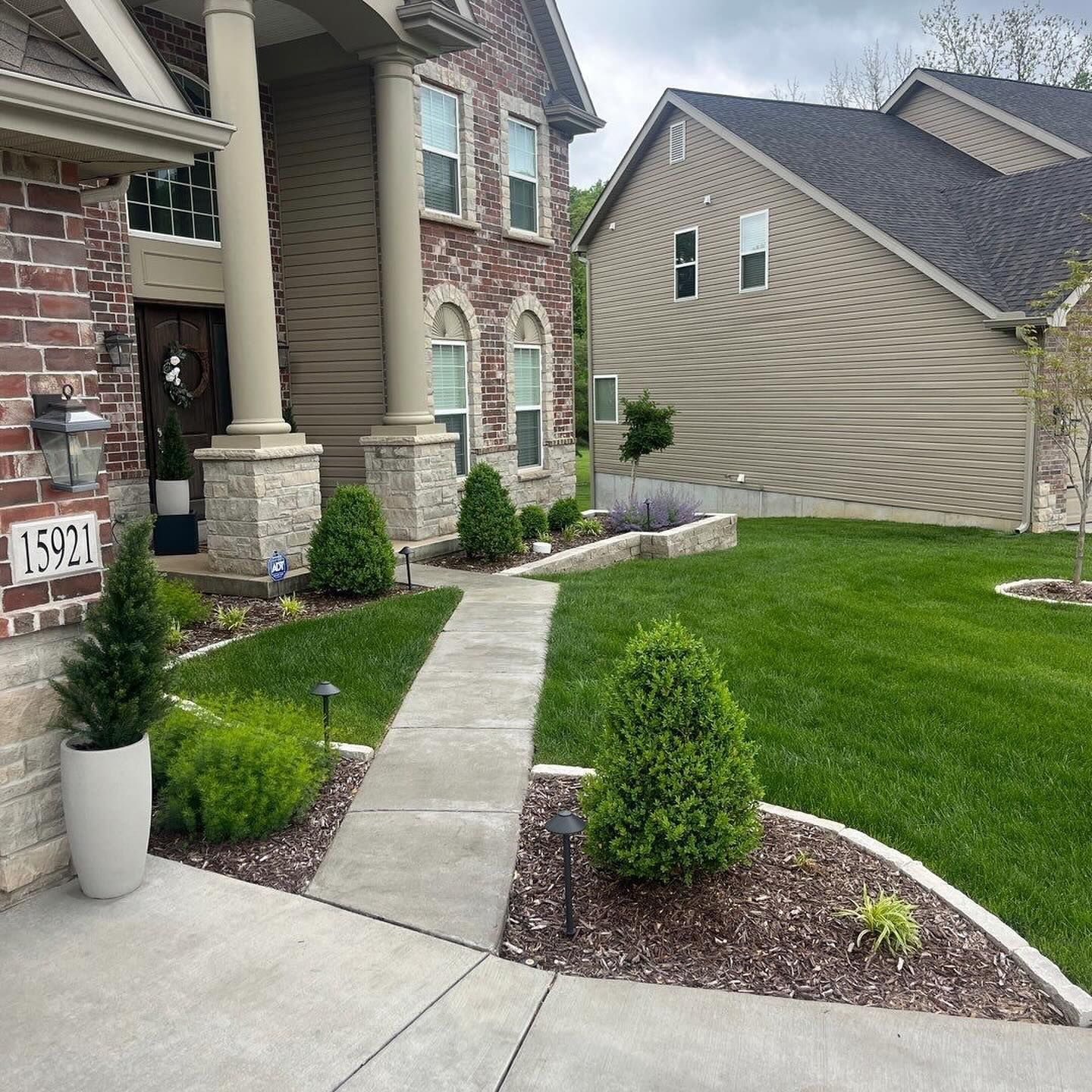A brick and stone house with a concrete walkway. Landscaping includes a manicured lawn