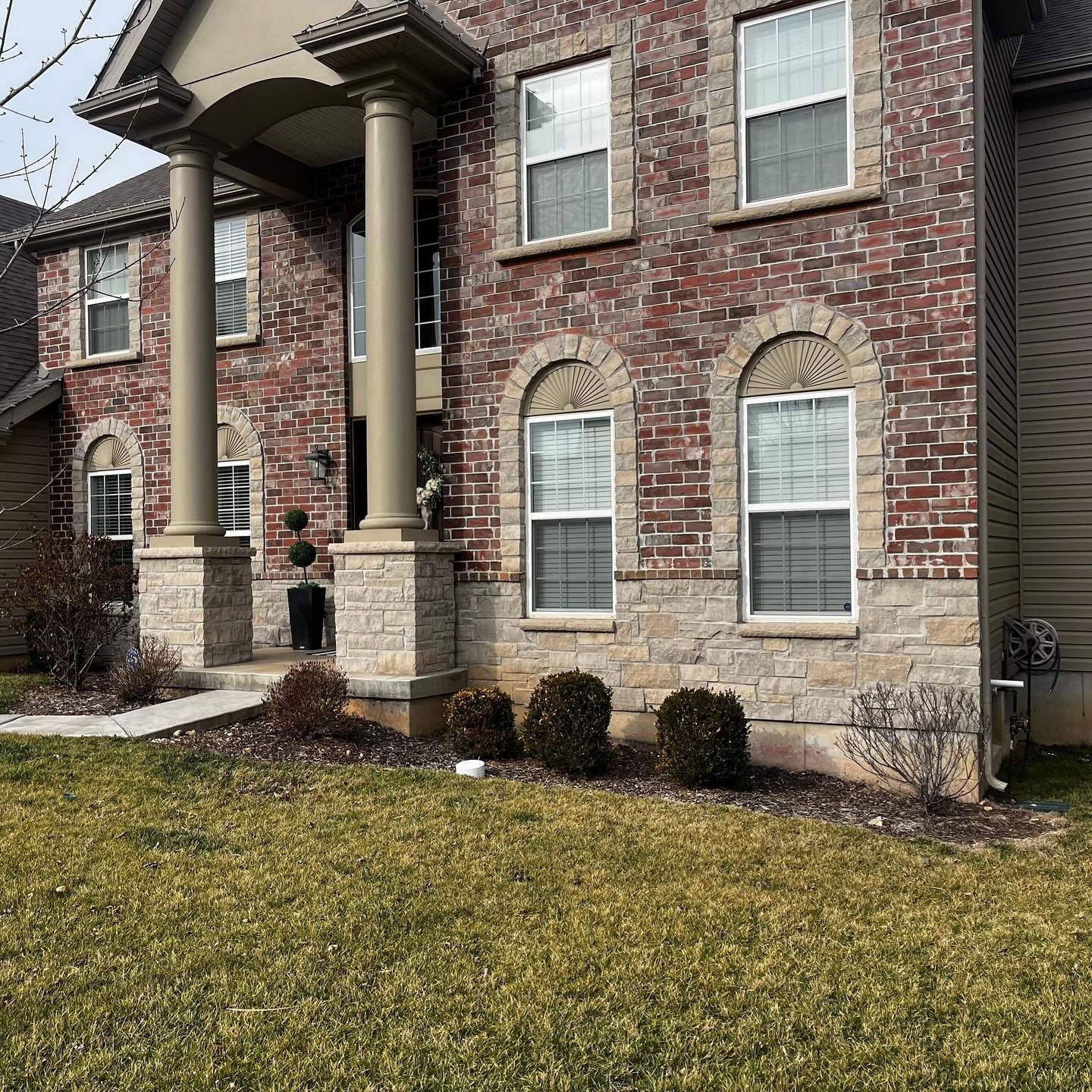 Brick house with columns, arched windows, and a grassy lawn. The house is red brick with tan stone accents.