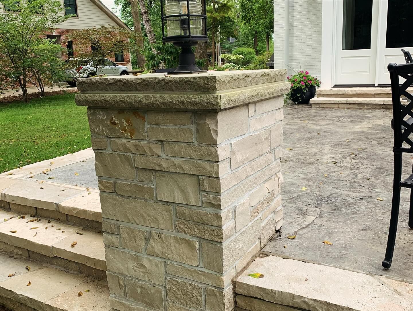 Stone pillar with a lamp on top, beside a patio with steps and a house in the background.