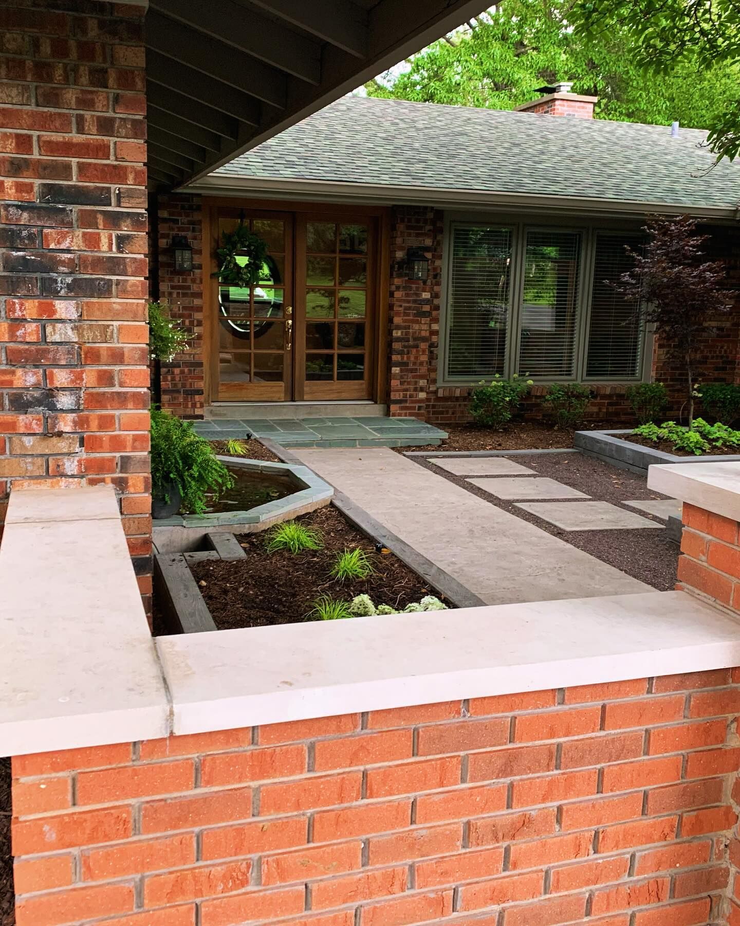 Brick home exterior with a walkway and landscaping. Wooden doors with glass panels lead to the entrance.
