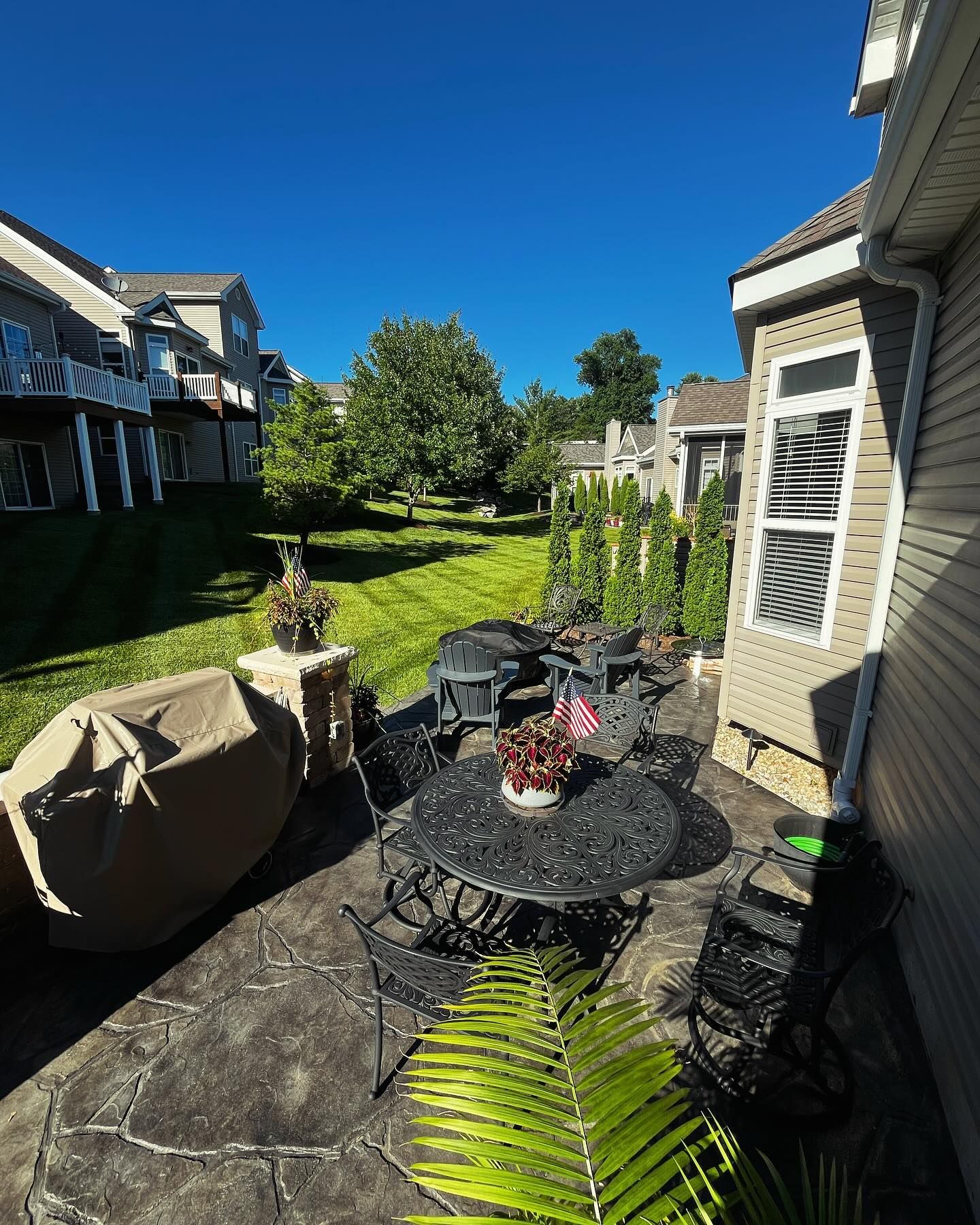 Patio with wrought iron furniture, green lawn, clear blue sky, and two-story houses.