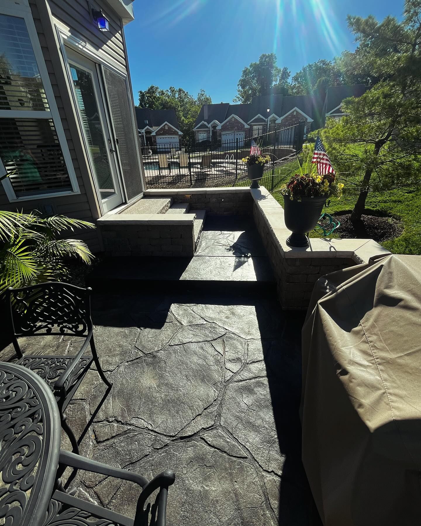 Patio with textured concrete, steps, and a retaining wall. Includes a grill cover, outdoor furniture, 