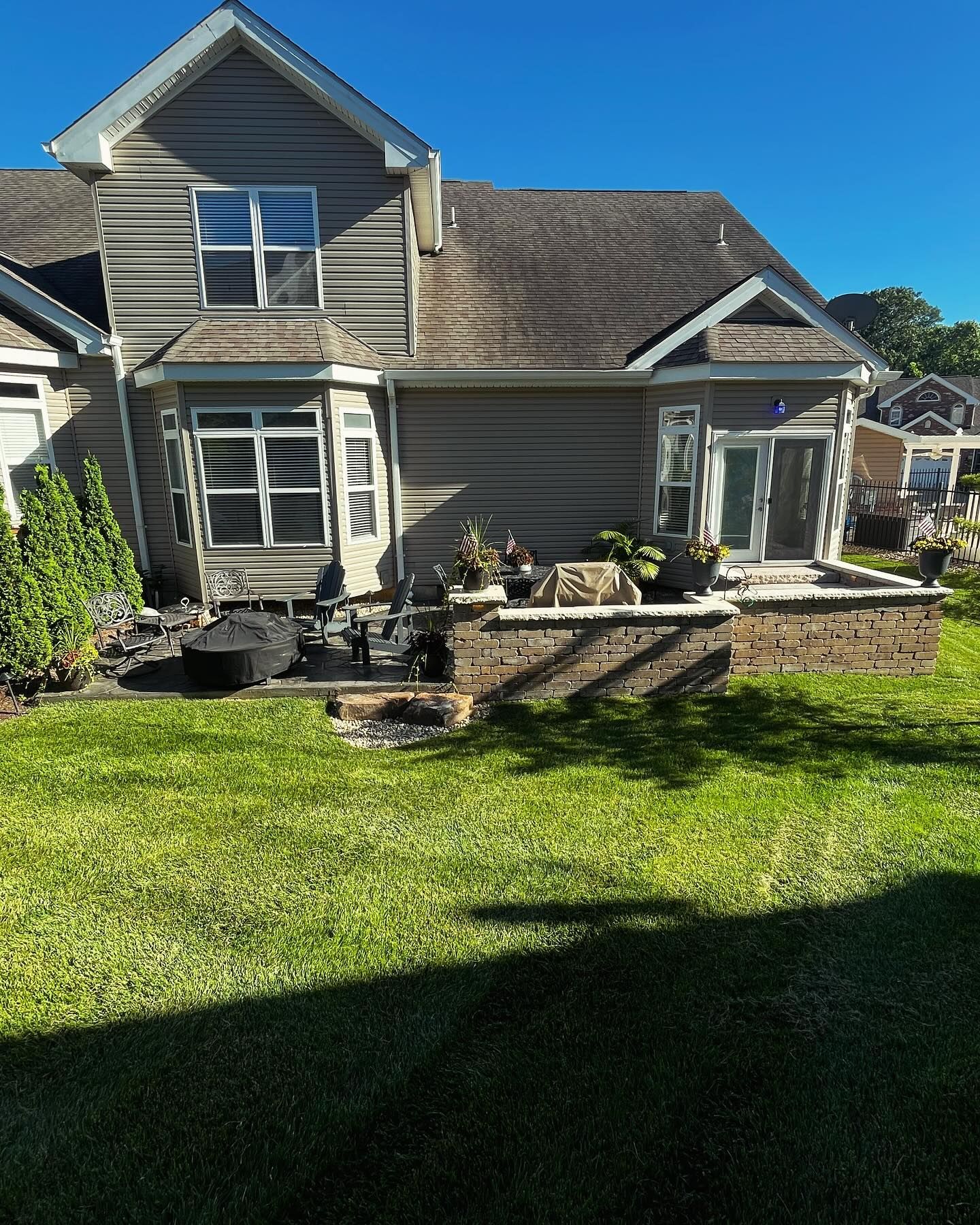 A two-story house with brown siding and a brick patio, viewed from a green lawn on a sunny day.