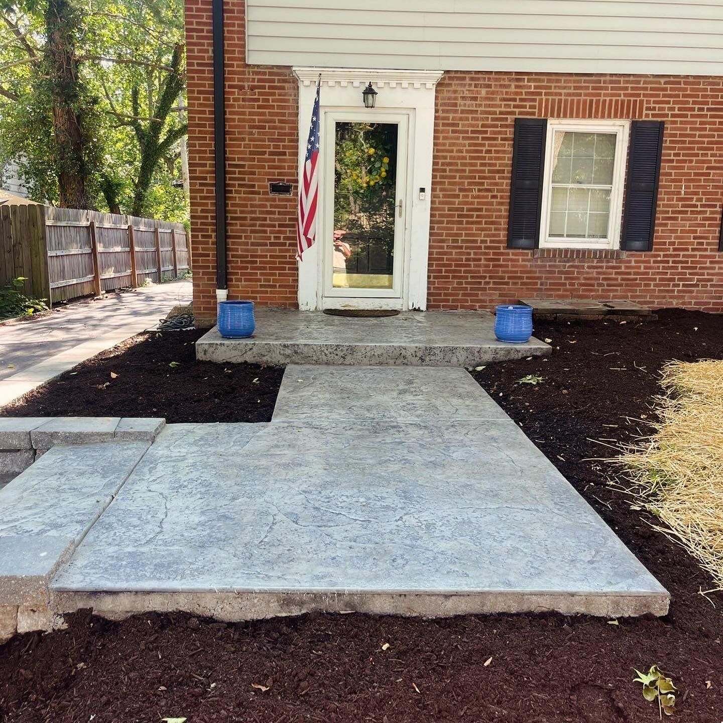 Brick house with a concrete path and porch, an American flag hangs in the doorway. 
