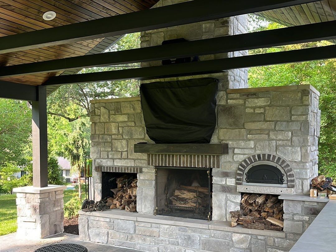 Outdoor stone fireplace with wood storage and a pizza oven under a covered patio.