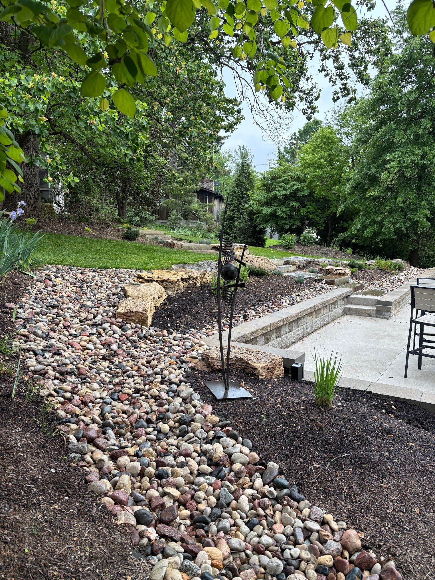 A landscaped backyard features a dry creek bed with stones, leading up to a patio with stone retaining walls.