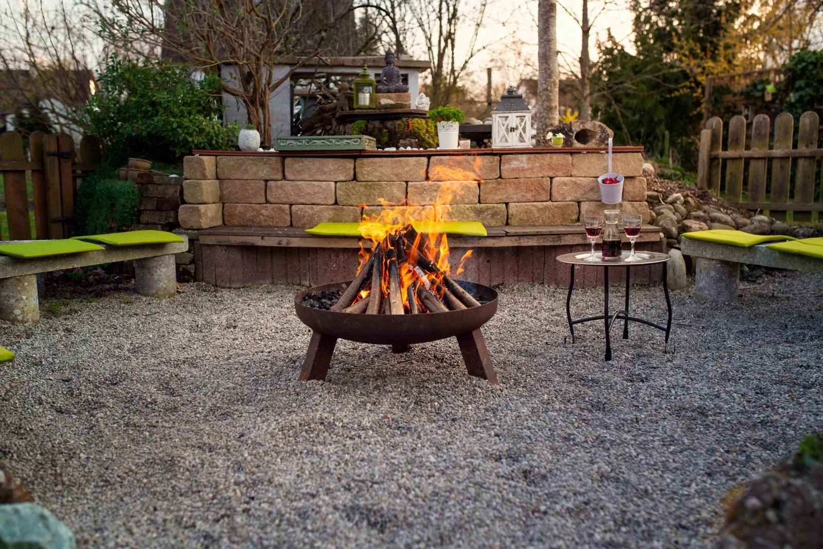 A fire pit with burning flames in a gravel-covered patio with seating.