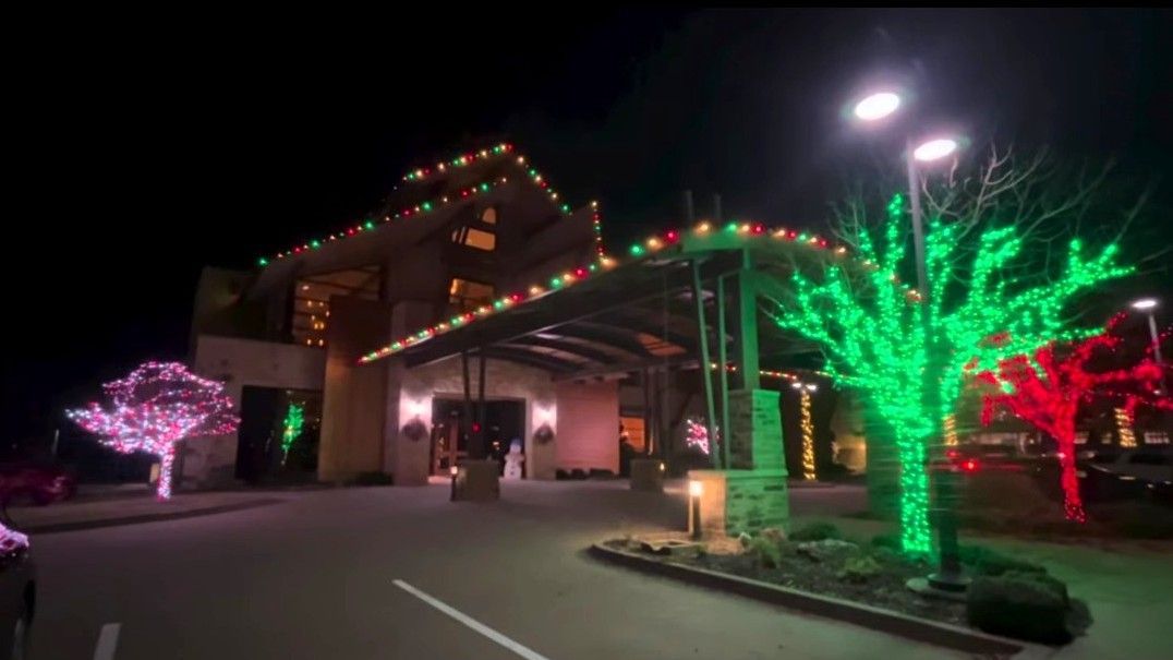 Building entrance decorated with red, green, and white Christmas lights. Trees are illuminated in pink, green, and red.