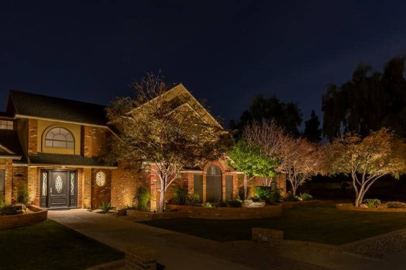 A large brick house is lit up at night with trees in front of it.