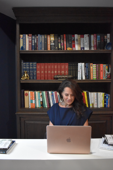 Woman working on a laptop in front of a bookcase filled with books.