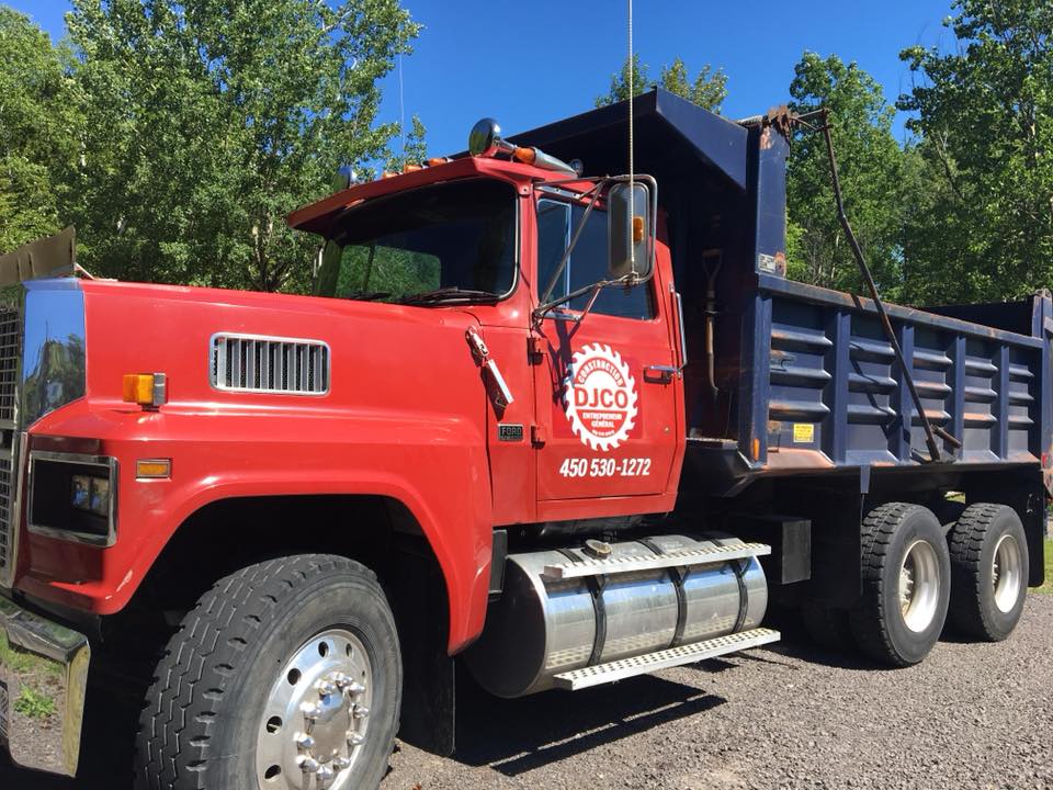 un camion à benne rouge est garé dans un terrain de gravier