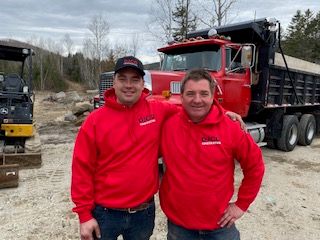 deux hommes de DJCO Construction posent pour une photo devant un camion-benne.