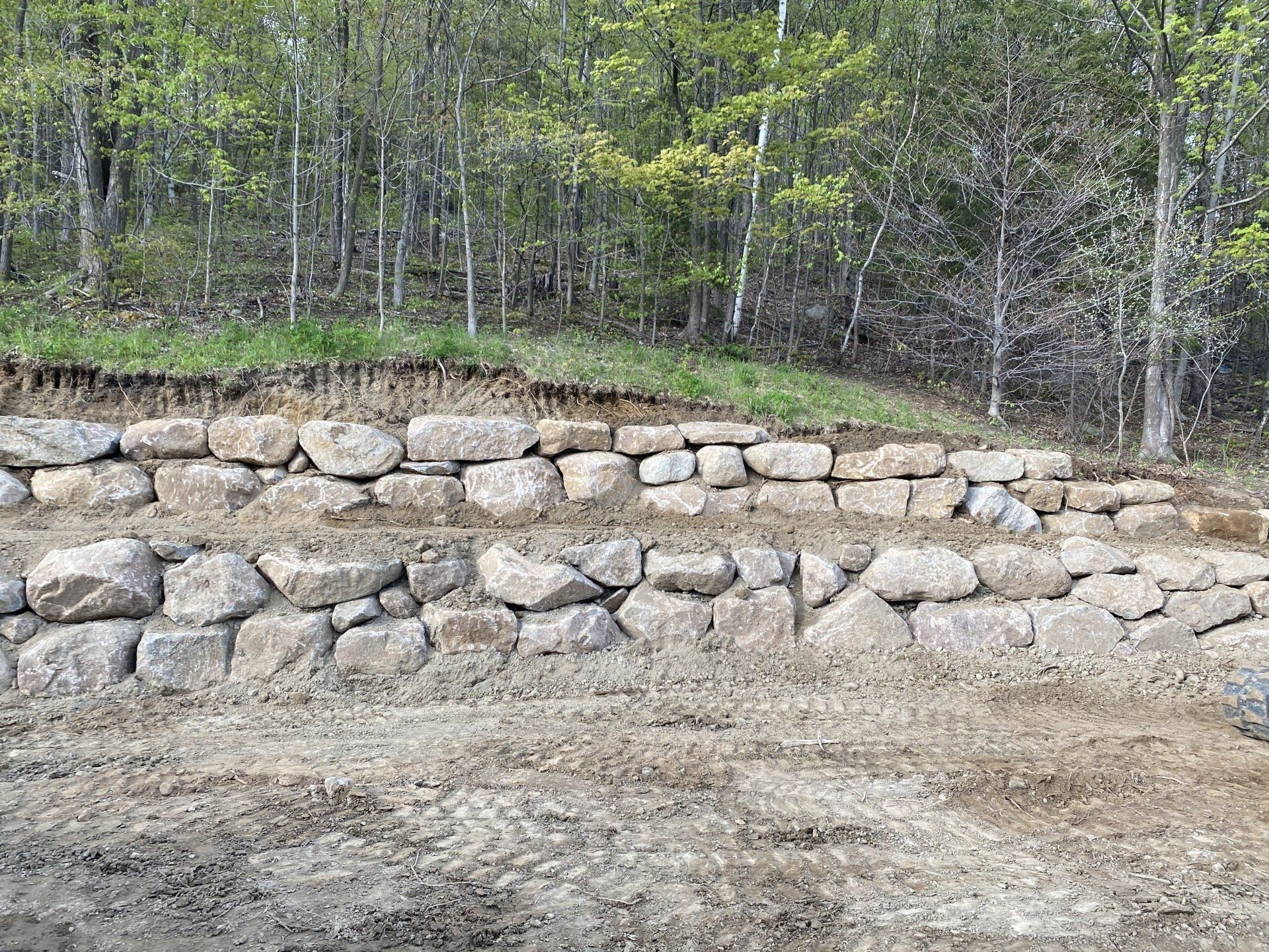 un mur de pierre est en train d être construit au milieu d un champ de terre.