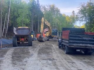 un camion à benne basculante roule sur un chemin de terre à côté d un chantier de construction.