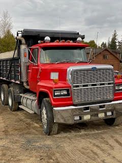 un camion à benne rouge est garé dans un champ de terre.