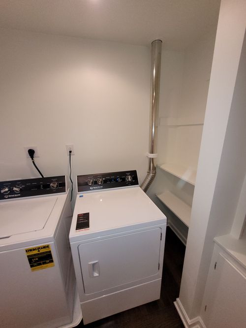 A white dryer and washing machine in a laundry room with a silver exhaust pipe.