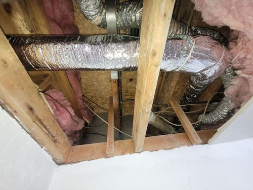 A view into an attic showing ductwork, pink insulation, and wooden framing.
