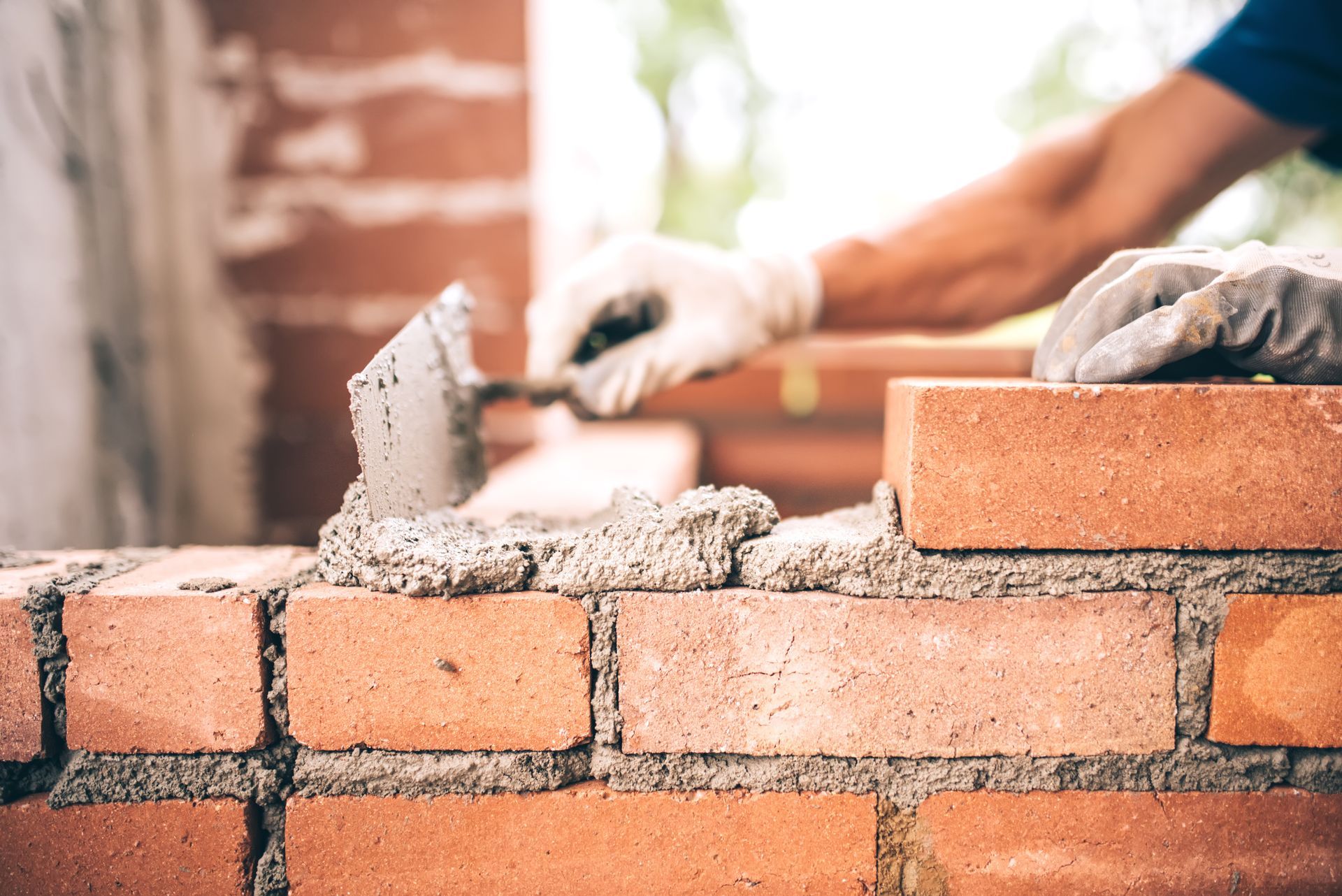 A masonry contractor installing brick masonry on the exterior wall with a trowel and putty knife.
