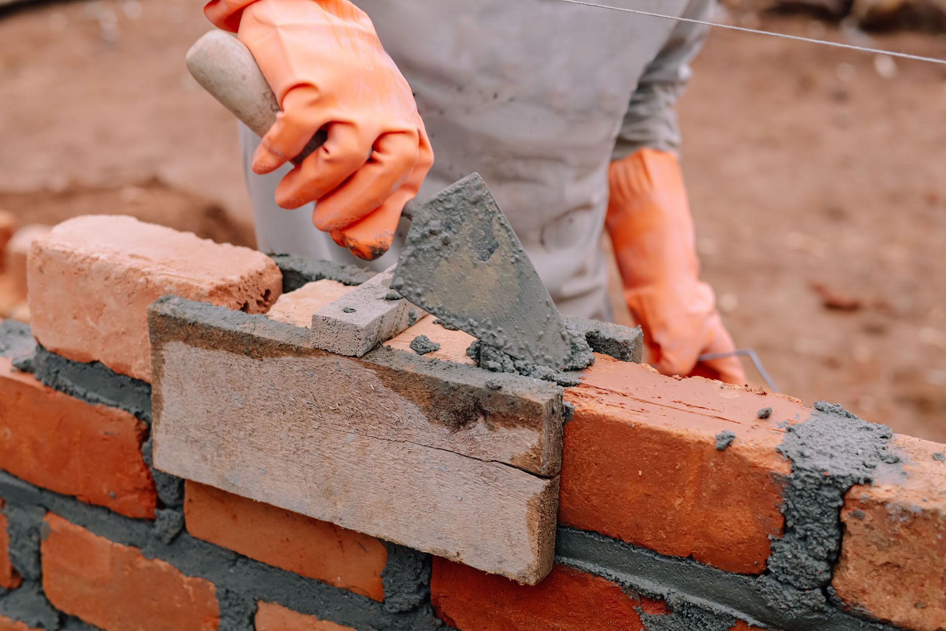 Mason is laying bricks with a trowel and mortar.
