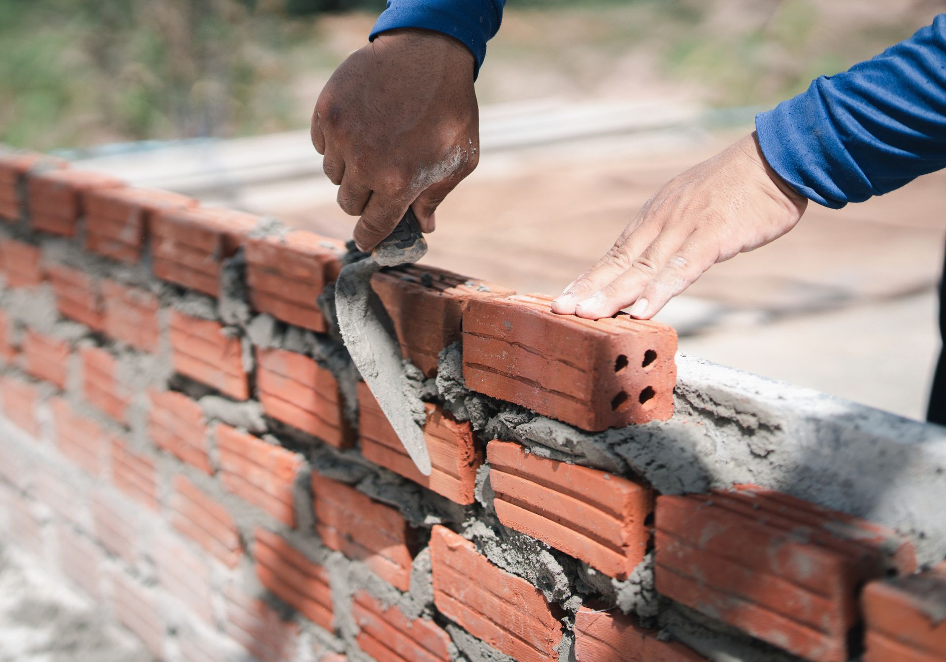 Close-up of a contractor’s hands as they install red bricks on a construction site.