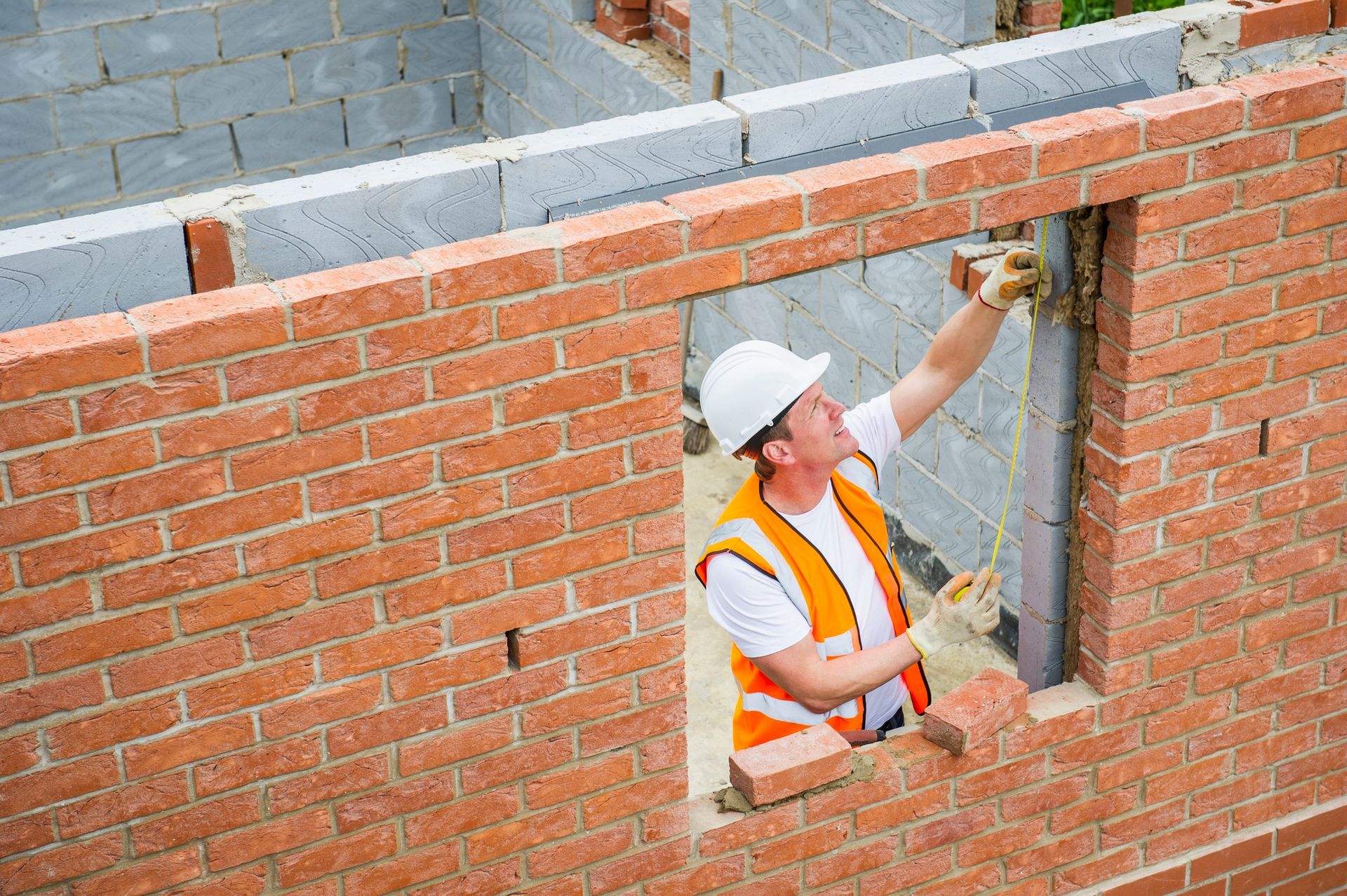 A worker is using a measuring tape to lay some bricks.