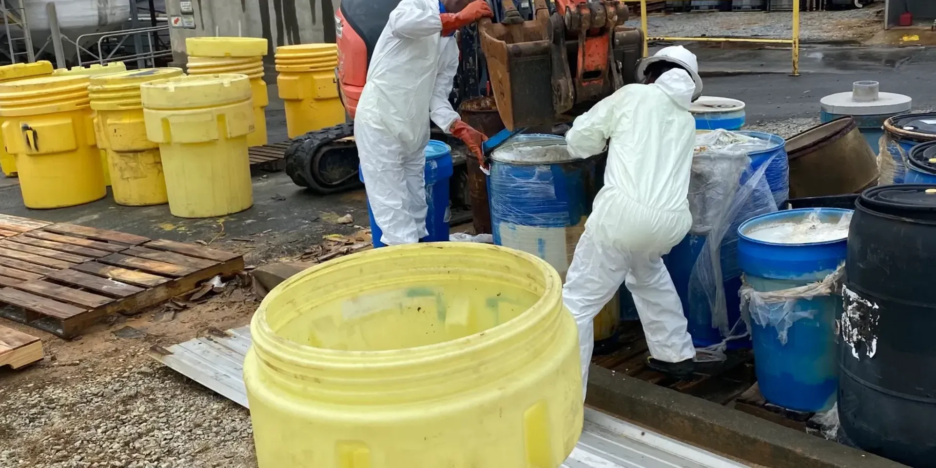 A group of people in protective suits are working on barrels.