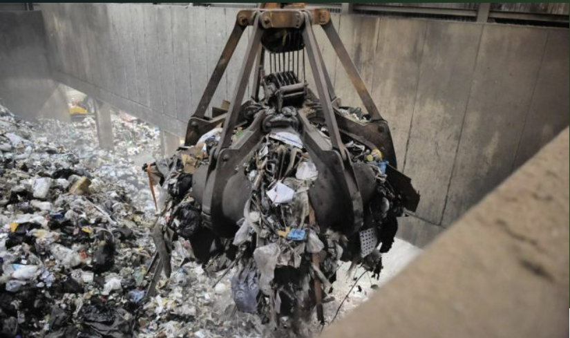 A large crane is reaching into a pile of trash.