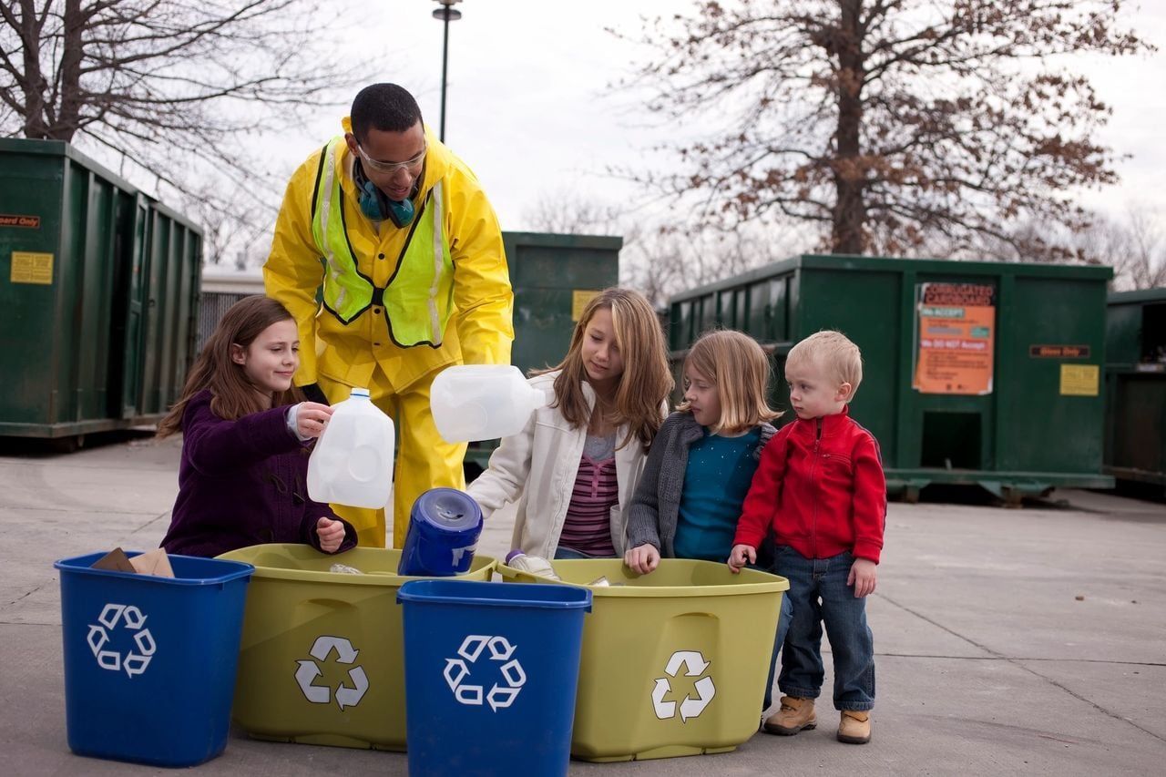 A group of children are standing around recycling bins.