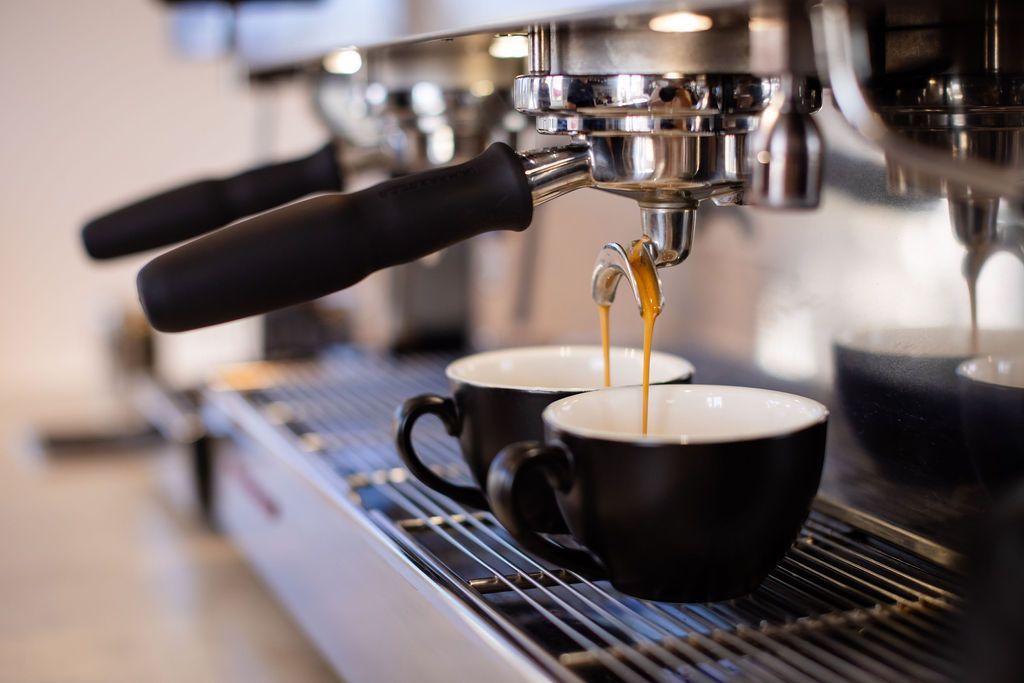 Two cups of coffee are being poured from a coffee machine.