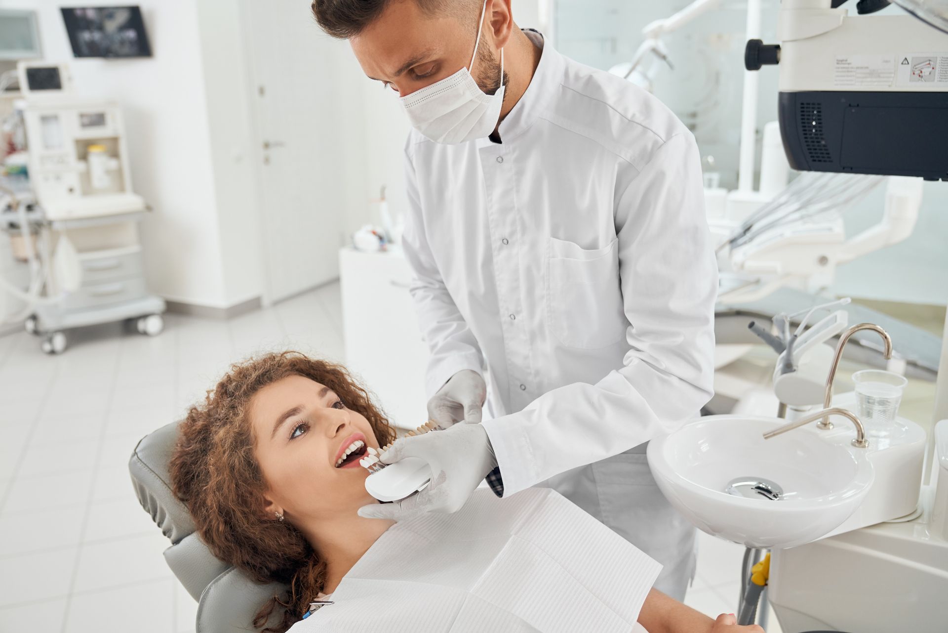 A woman is sitting in a dental chair while a dentist examines her teeth.