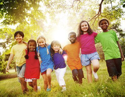 A group of seven children with arms linked, walking happily through a sunny, grassy park.