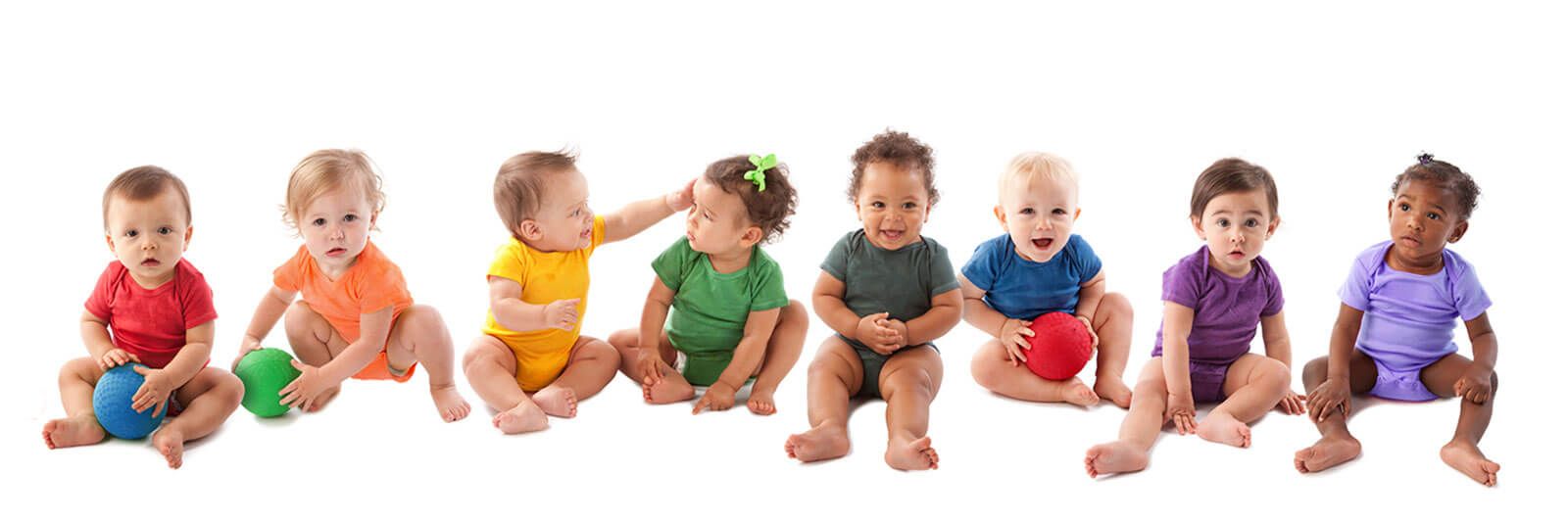 Eight babies in colored onesies sitting in a row against a white background, some playing with small balls.