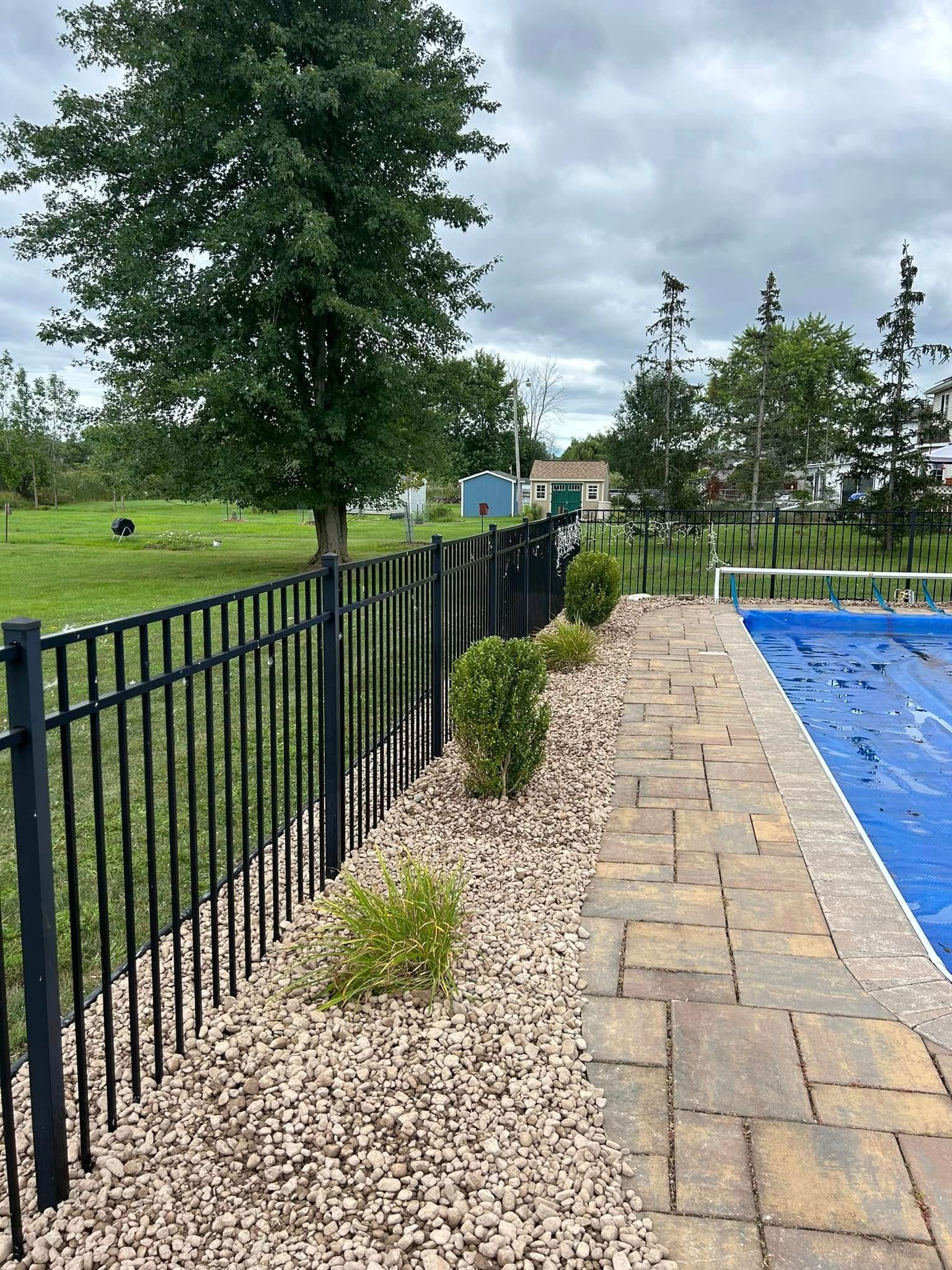 A fence surrounds a swimming pool with a blue cover on it.