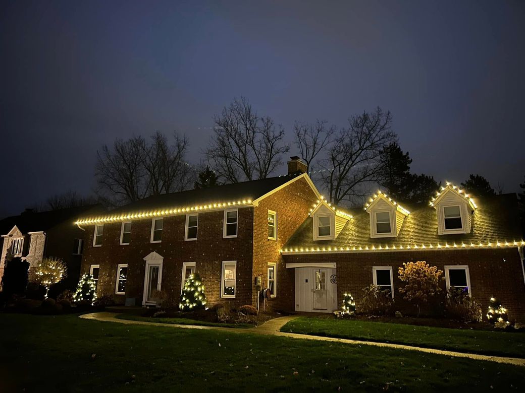 A large brick house is decorated with christmas lights at night.