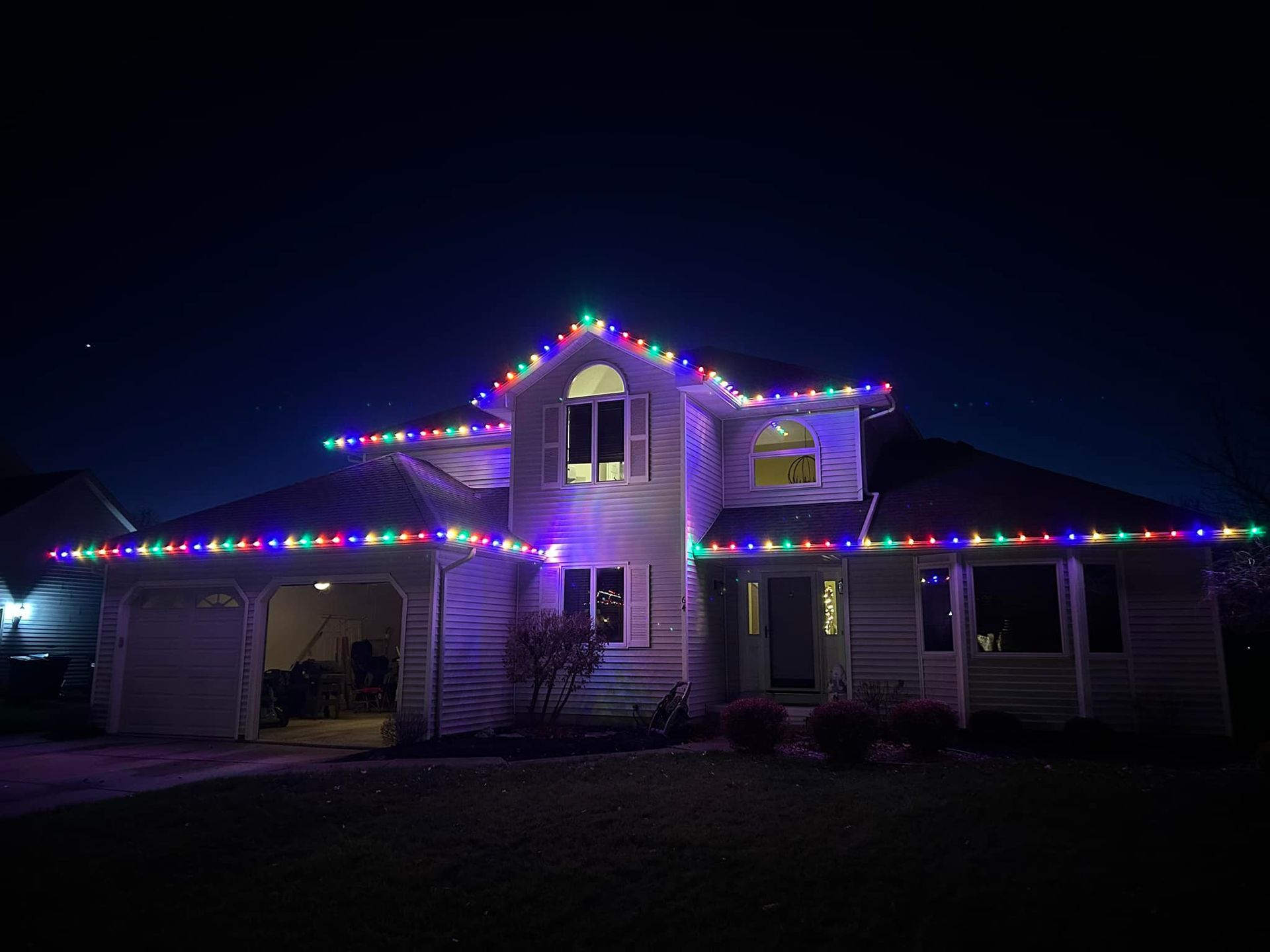 A large white house is decorated with christmas lights at night.