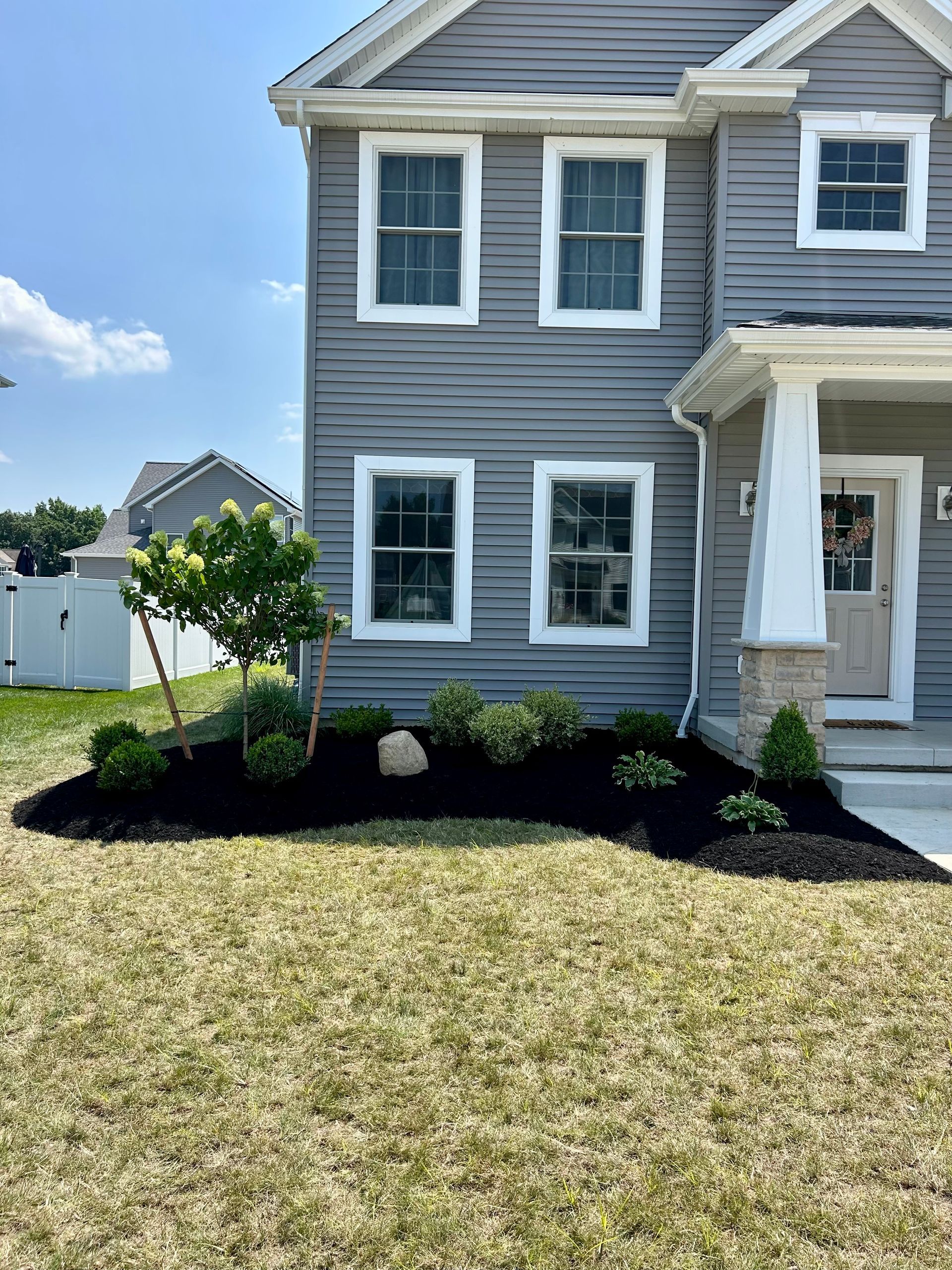 A gray house with white trim and a lush green lawn in front of it.