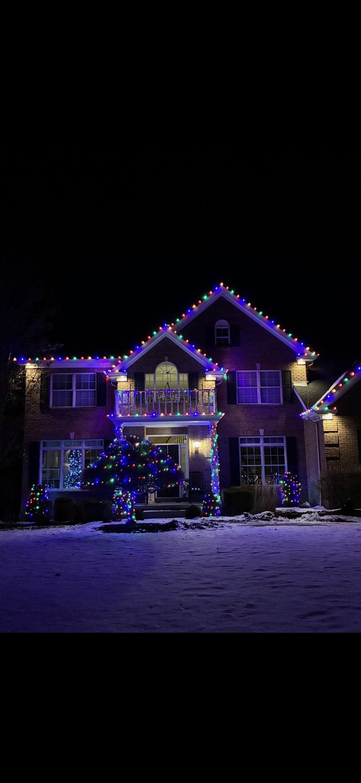 A large white house is decorated with christmas lights at night.