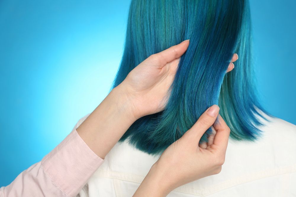 Unas manos apartan un mechón de cabello azul brillante sobre un fondo azul a juego.