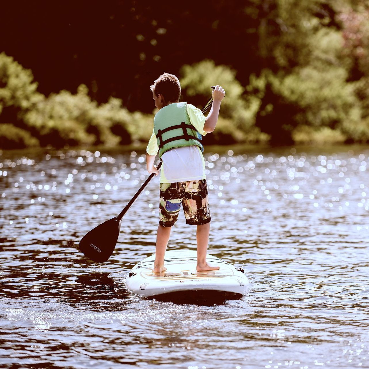 A young boy is standing on a paddle board in the water.