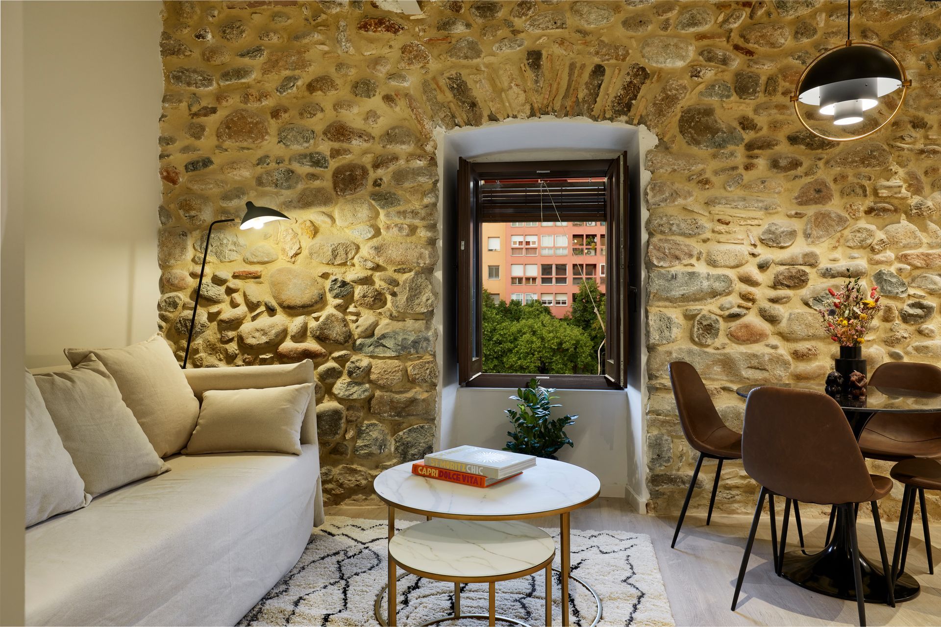 A living room with a couch , table , chairs and a stone wall.