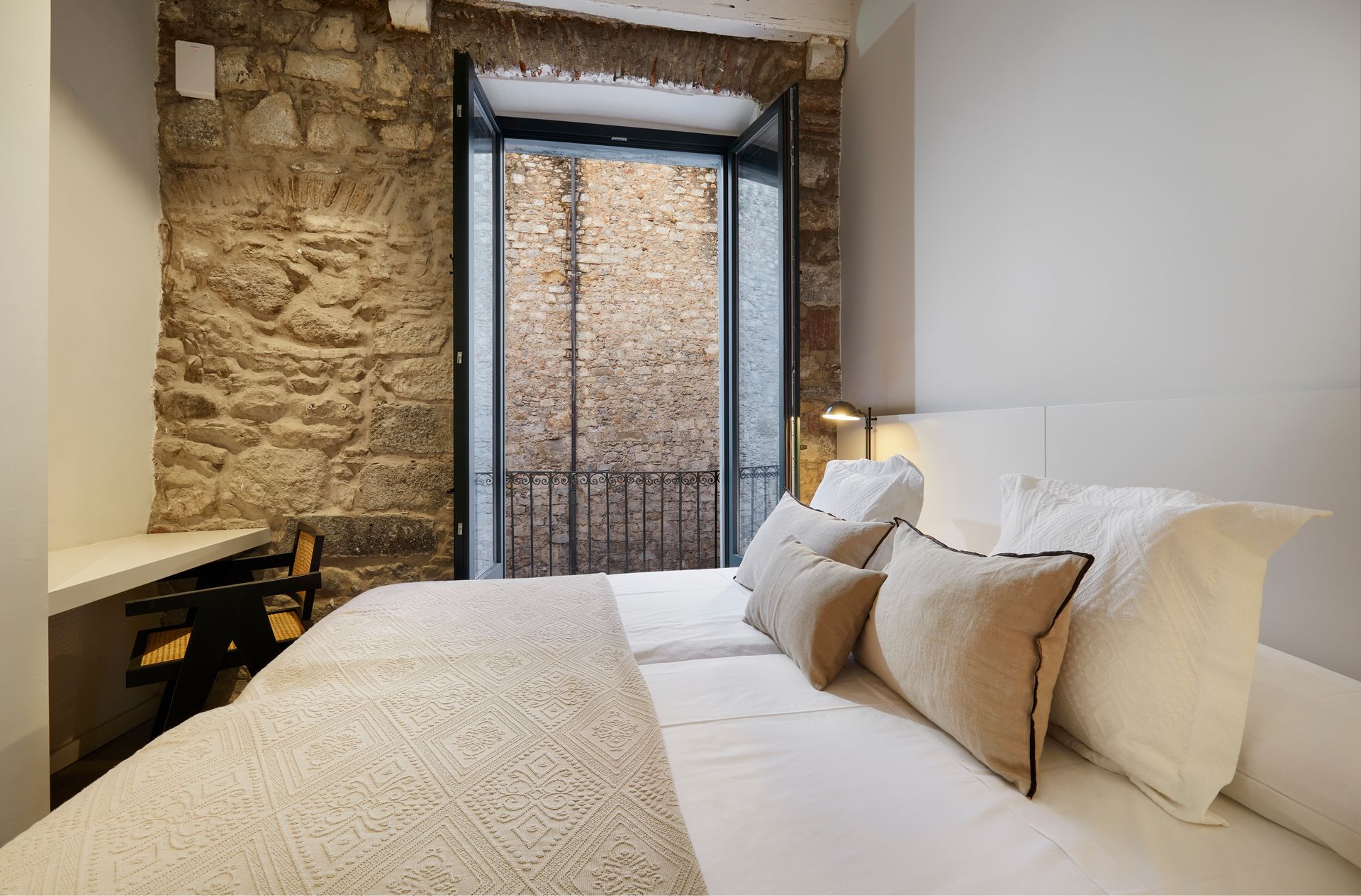 A bedroom with a bed and a balcony with a stone wall.