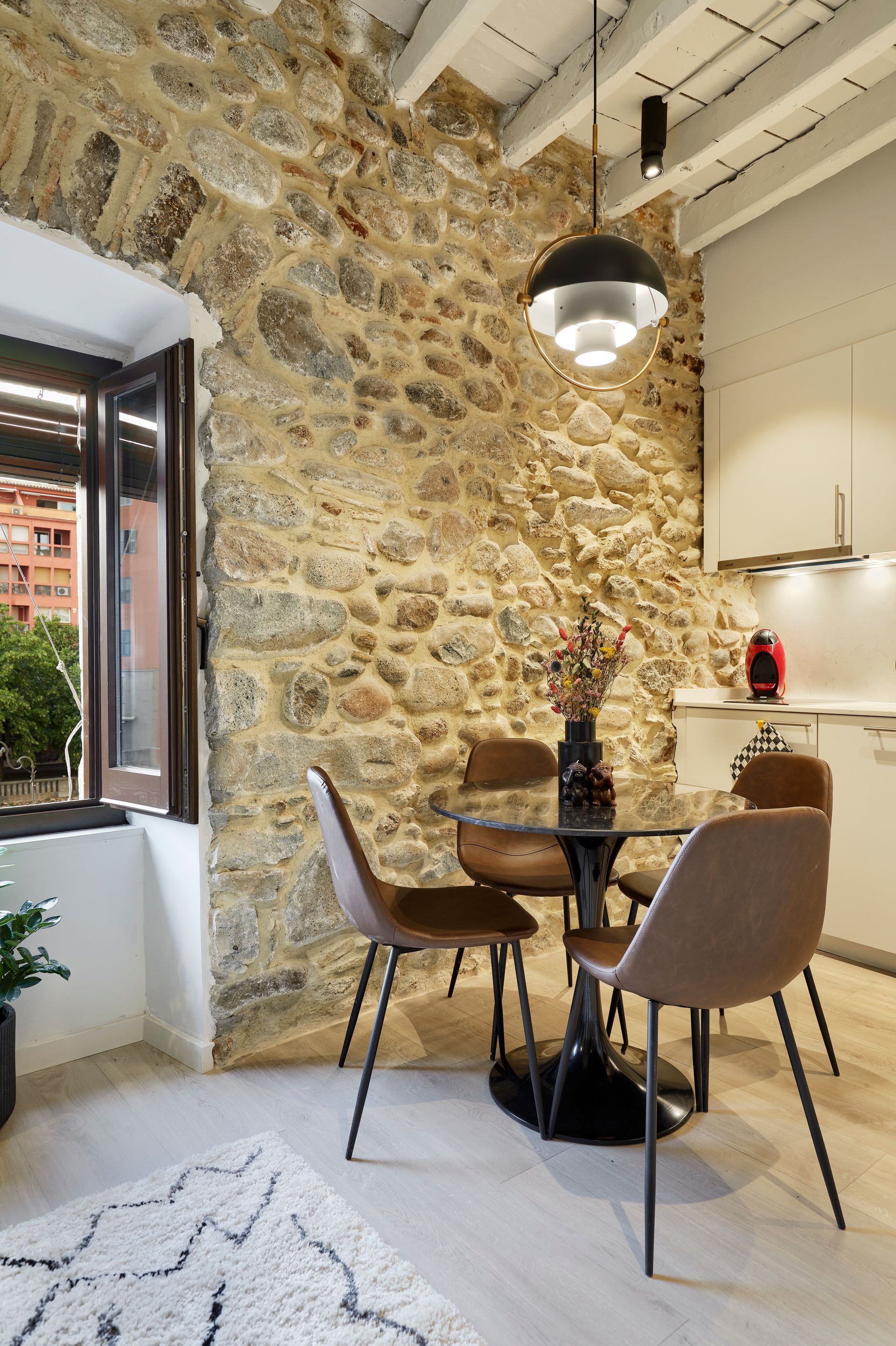 A dining room with a table and chairs in front of a stone wall.