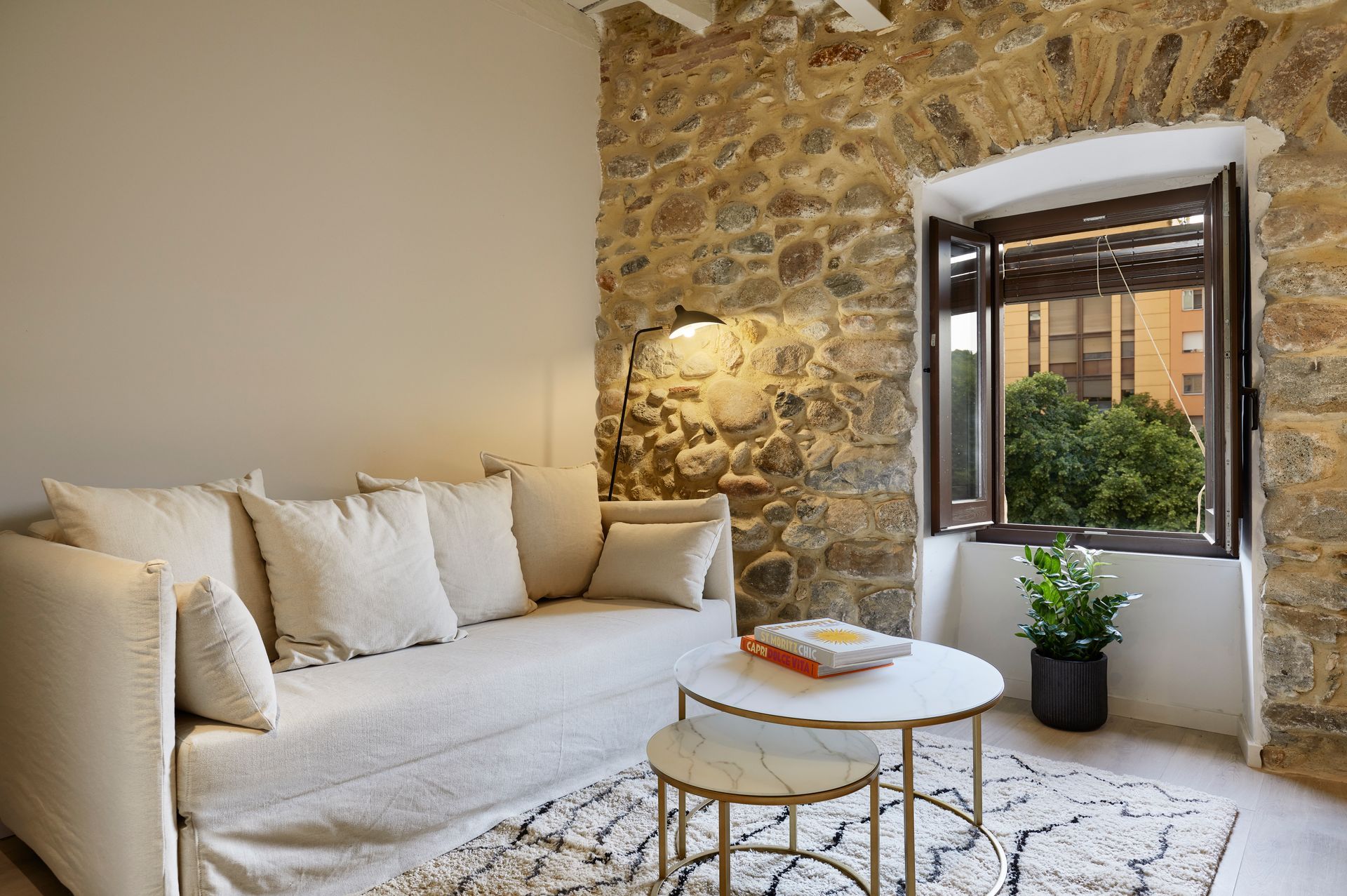 A living room with a couch , two coffee tables , and a stone wall.