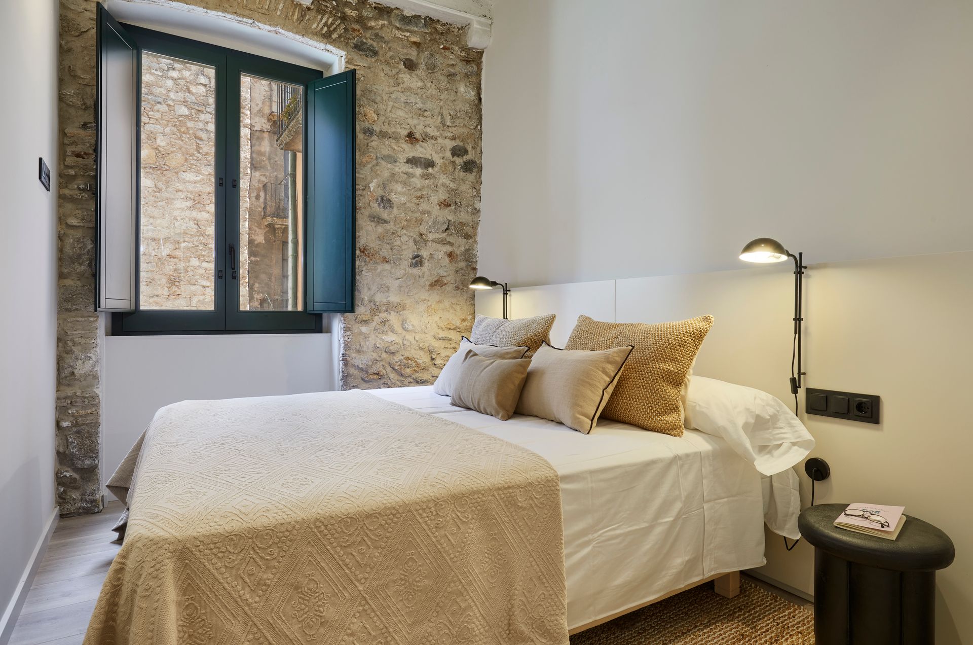 A bedroom with a bed , nightstand , lamp and window.