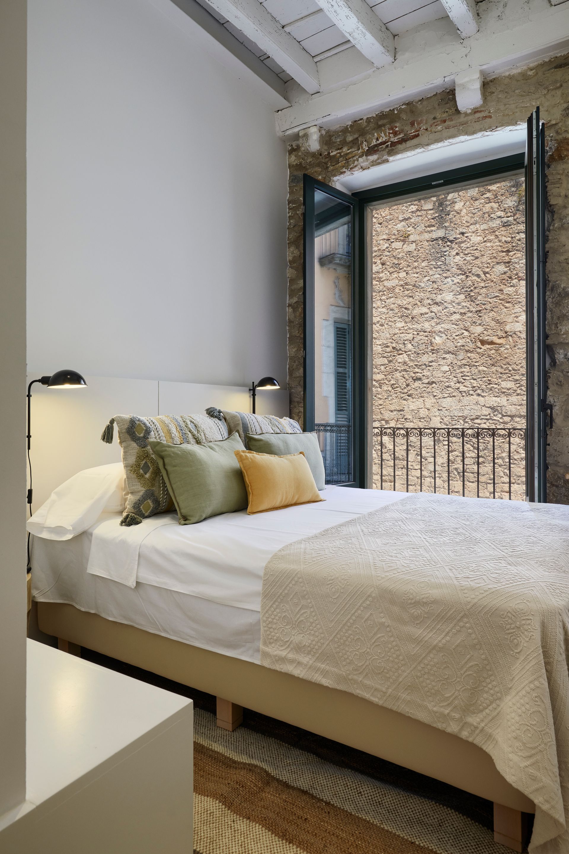 A bedroom with a bed and a balcony with a brick wall.