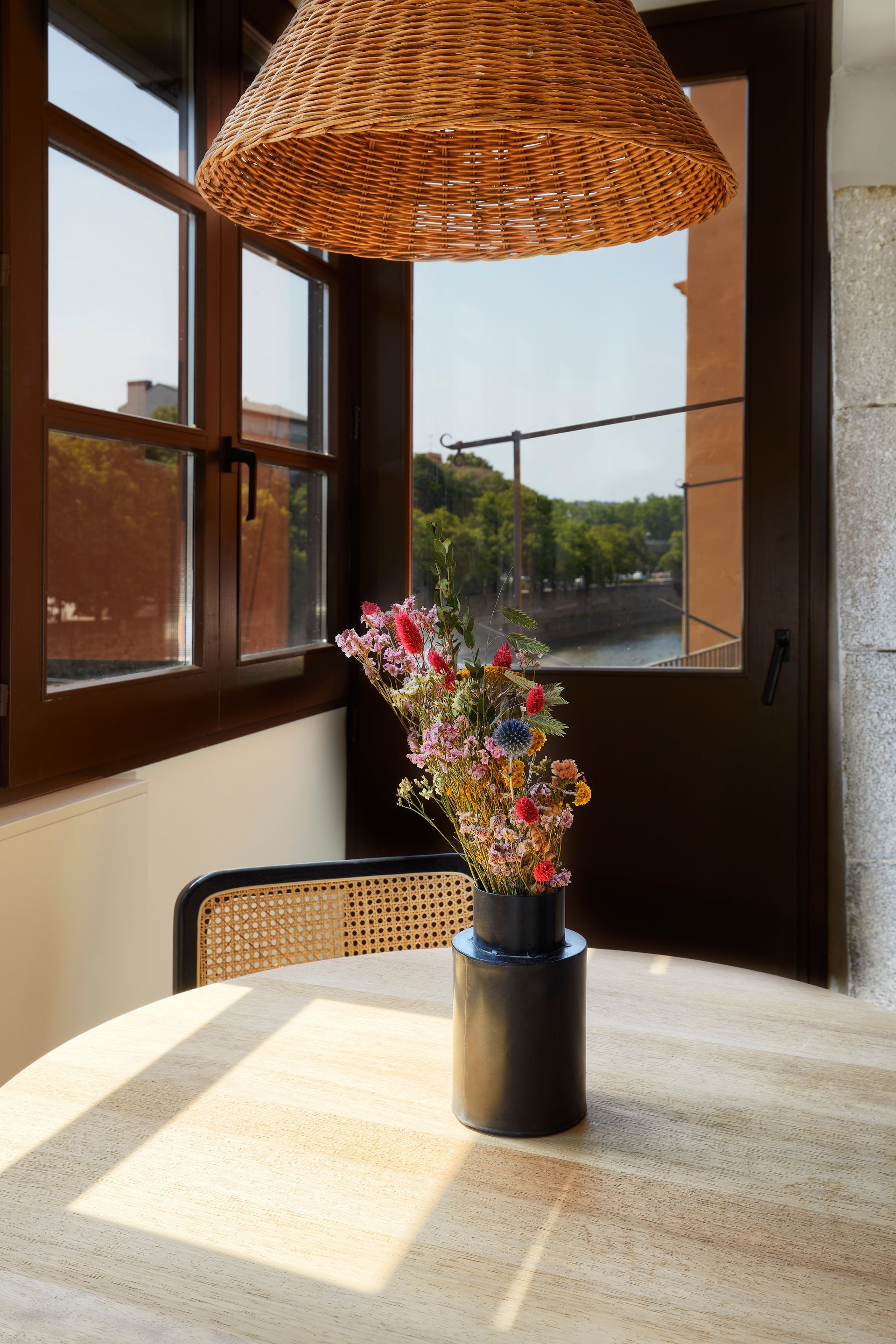 A vase of flowers is sitting on a table in front of a window.