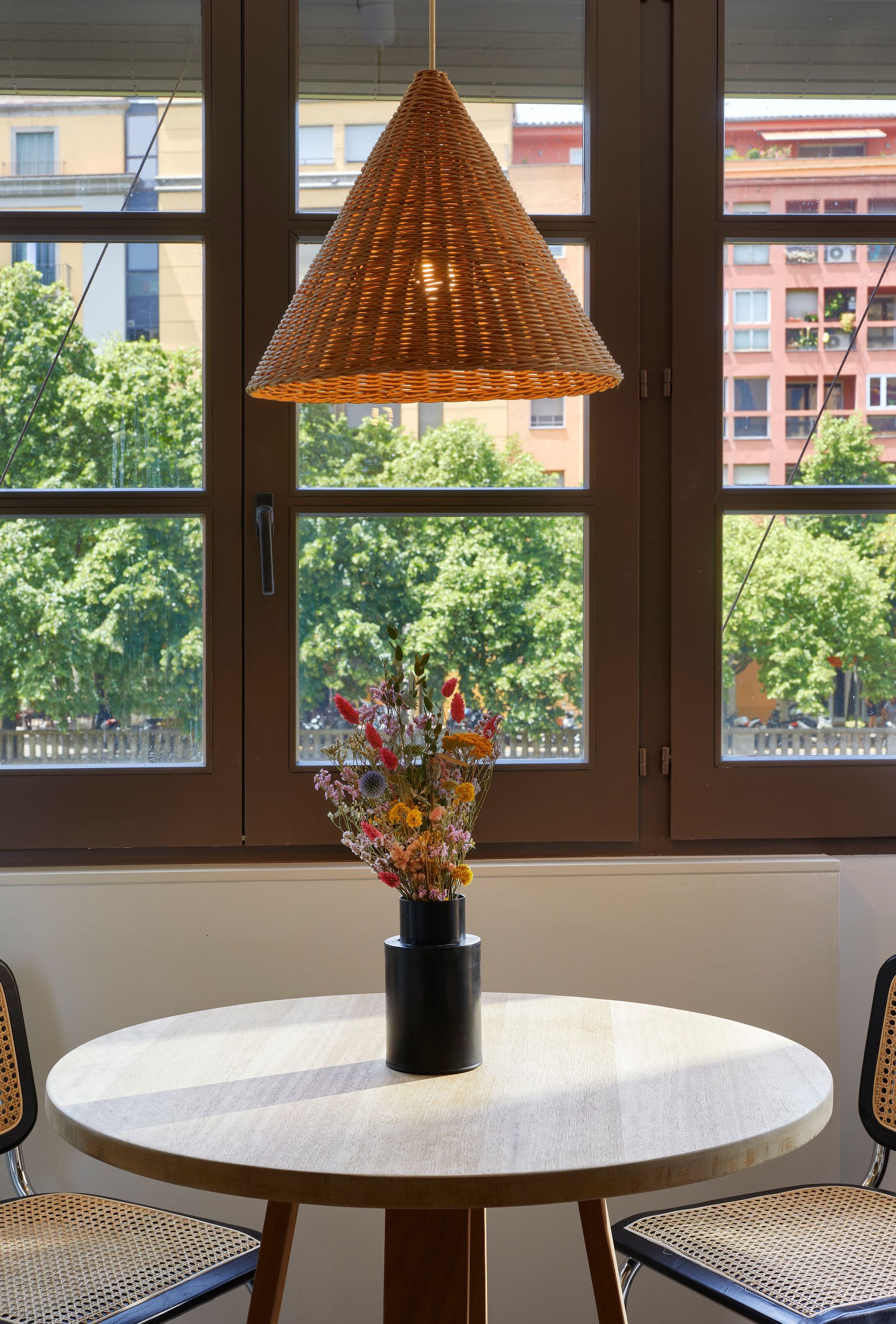 A table with a vase of flowers on it in front of a window.