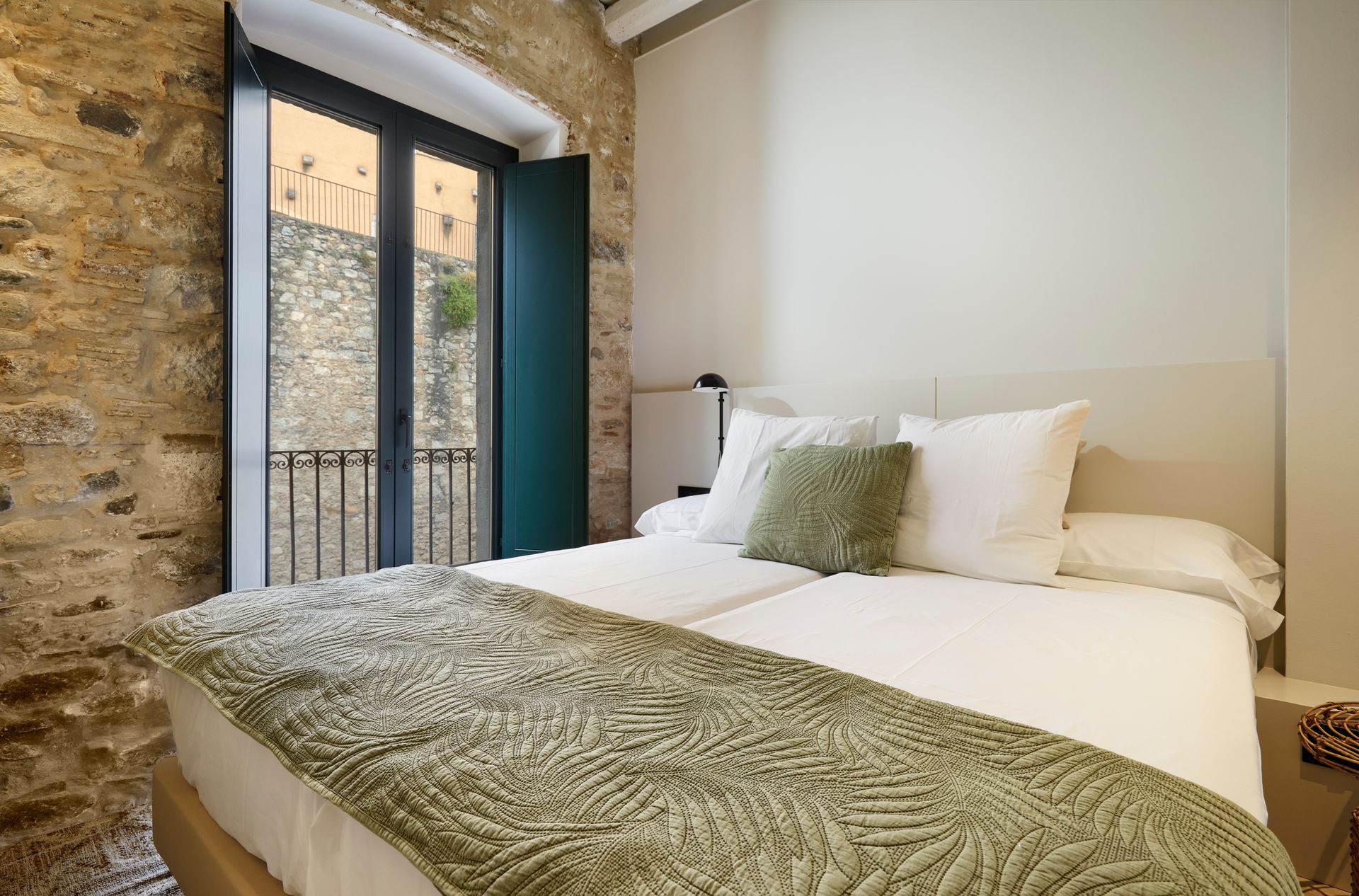 A bedroom with a bed and a window with a balcony.