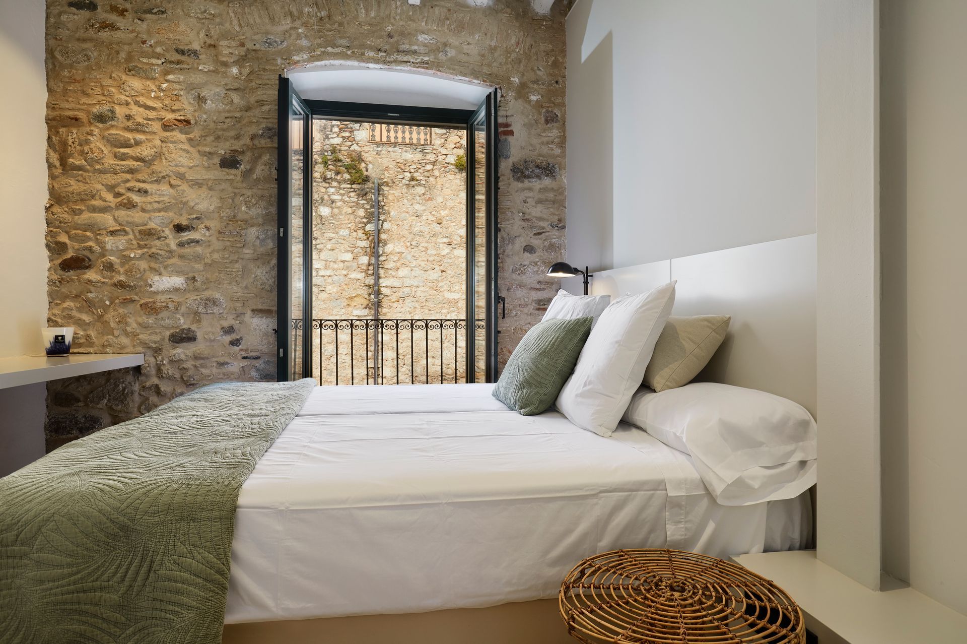 A bed with white sheets and pillows in a bedroom with a stone wall.